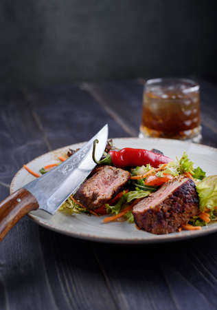 Tagliata of beef with salad on a white plate and a glass of whiskeyの写真素材