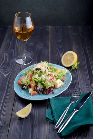 Caesar salad with salmon in a blue plate on a wooden table and a glass of wineの写真素材
