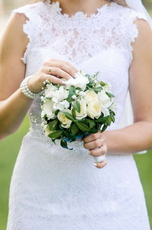 Wedding bouquet of white flowers and greenery in the hands of the bride in a white dressの写真素材