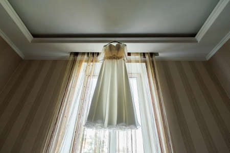 Bride's dress hanging on the rack near the window in the roomの写真素材