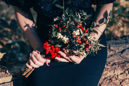 Bouquet of red, black and white berries in the hands of a girl in a black dress.Beautiful young girl in a black dress with a bright bouquet of berries in hands. Autumn bouquetの写真素材