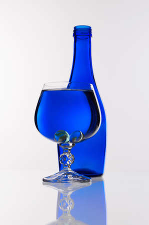 Transparent wine glass with water in front of a blue bottle on a white backgroundの写真素材