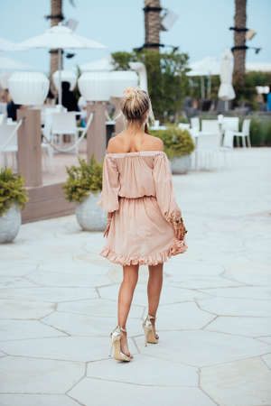 Beautiful young blond woman in a short translucent dress walking. Elegant luxury sexy blonde model wearing dress goes through the streets for shoppingの写真素材