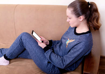 Beautiful young woman sitting on a sofa, using a smartphone and texting. Relaxing on the couch at home. Technology and communication conceptの写真素材