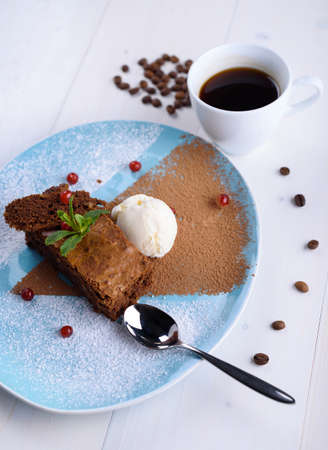 Chocolate brownie with ice cream on a blue plate next to a cup of coffeeの写真素材