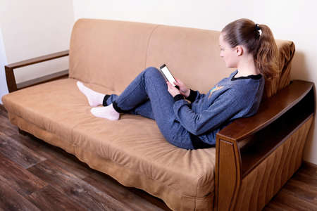 Beautiful young woman sitting on a sofa, using a smartphone and texting. Relaxing on the couch at...