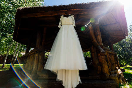 Beautiful wedding dress hanging on the wooden arbor next to the birch outdoorsの写真素材