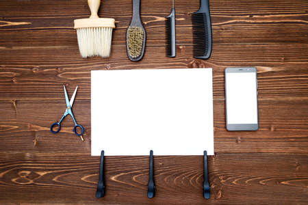 Hairdresser tools on wooden background. Blank card with barber tools flat lay. Top view on wooden table with scissors, comb, brush and hairclips with empty white paper and phone, free spaceの写真素材