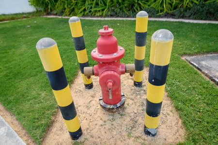 Red fire hydrant surrounded by yellow-black pillars against a green lawn. Prevention systemの写真素材