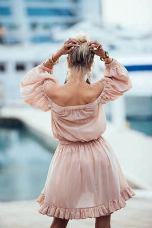 Beautiful young blond woman in a short translucent dress walking at beach resort. Elegant luxury sexy blonde model wearing dressの写真素材