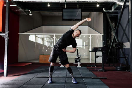 Young man preparing muscles before training. Muscular athlete exercising in gym. Fit man stretching....