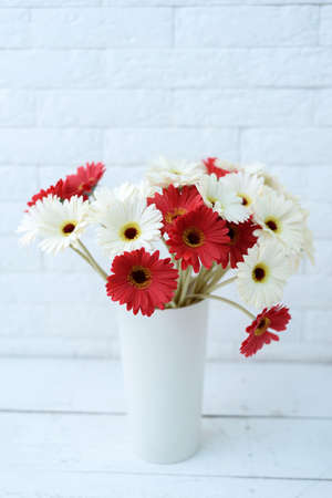 White and red gerberas in white vase near white brick wallの写真素材