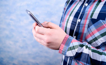 Young man in a plaid shirt using a smartphone and texting. Technology and communication conceptの写真素材