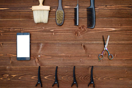 Hairdresser tools on wooden background. Top view on wooden table with scissors, comb, brush and hairclips with phone, free spaceの写真素材