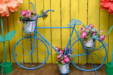 Vintage decorative metal blue bicycle flower-stand with pink peonies on yellow backgroundの写真素材