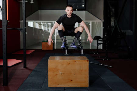 Fit young man jumping onto a box as part of exercise routine. Man doing box jump in the gym. Athlete is performing box jumpsの写真素材