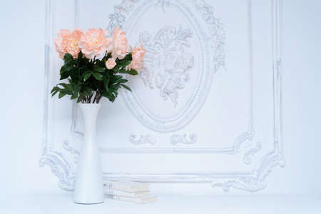 Artificial pink peonies in a white vase next to white books. Composition of flowers in a white vaseの写真素材
