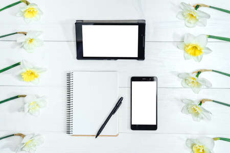 Top view on table with narcissus, empty diary, pencil, tablet and phone, free space. Yellow narcissus on white wooden background. Blank card flat layの写真素材