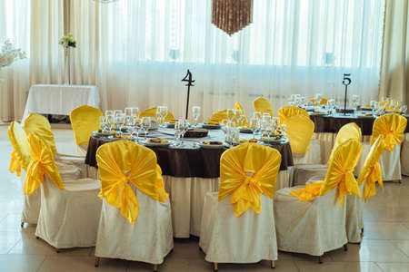Chairs with yellow cloth and table for guests served for wedding banquet with numbers. Dinner table...