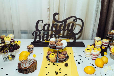 Holiday candy bar in yellow and brown color. Wedding candy bar served with cupcakes, cake pops, desserts in glasses, lemons and coffee beansの写真素材