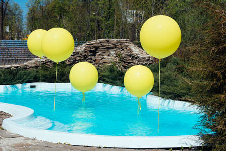 Pool with big yellow balloons outdoor. Poolside party. The balloons on water. Decorations for wedding ceremony by the pool with blue waterの写真素材