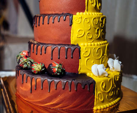 Round multi tiered  yellow and brown wedding cake with strawberries, roses and chocolate icingの写真素材