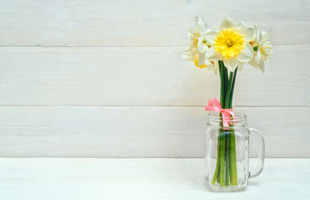 Bright yellow daffodils in vase on white wooden table with copy space. Yellow and white narcissus....