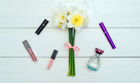Top view on white wooden background with ?osmetics: mascara, lip gloss, lipstick and perfume around bouquet of narcissus. Liquid Lipstickの写真素材