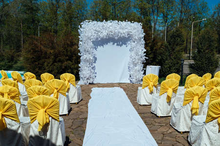 Place for wedding ceremony with white arch and yellow chairs for guests. Beautiful wedding archway with chairs on each side outdoorsの写真素材