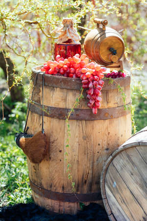 Old wooden wine barrel with bottle of wine and grapes on it. Wedding decorations outdoorsの写真素材