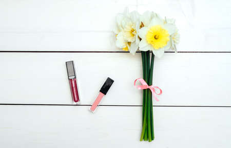 Top view on white wooden background with lip gloss and bouquet of narcissus. Liquid Lipstickの写真素材