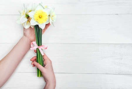 Yellow bouquet of narcissus in woman hands on white background. Flat lay, top view, copy space. Floral backgroundの写真素材