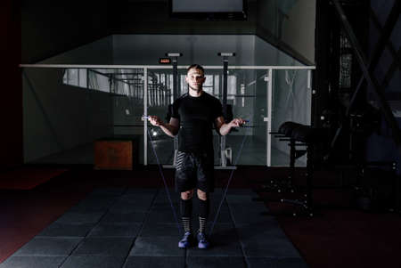Muscle man skipping rope. Athlete using jump ropes for the workout in a cross-training gym. Man jumping rope at the gymの写真素材
