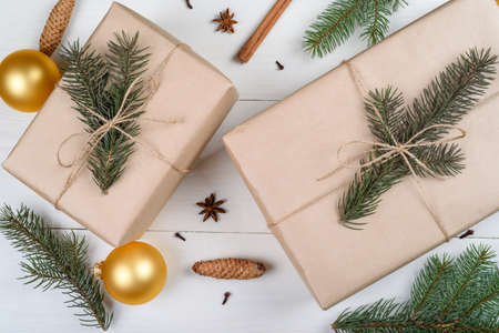 Christmas background with gift boxes wrapped in kraft paper, fir tree branches, golden glass balls, pine cones, cinnamon sticks and stars anise on white wooden background. Flat lay, top viewの写真素材