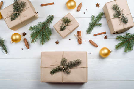 Christmas background with gift boxes wrapped in kraft paper, fir tree branches, golden glass balls, pine cones, cinnamon sticks and stars anise on white wooden background. Flat lay, top viewの写真素材