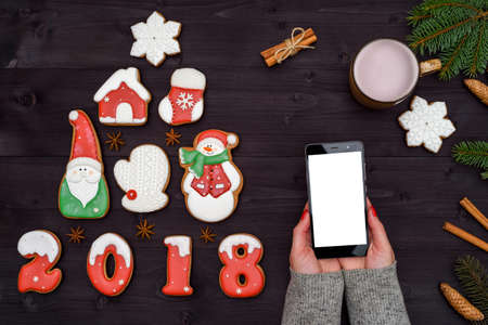 Mobile smart phone with blank screen for app presentation in woman hands, copy space. Christmas background with gingerbread cookies and cup of cocoa. Flat lay, top view. Application mock up templateの写真素材