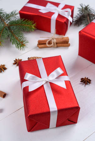 Christmas background with red gift boxes, fir tree branches, pine cones, cinnamon sticks and stars anise. Red Christmas gift boxes on white wooden background. Holiday greeting cardの写真素材