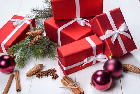Christmas background with red gift boxes, fir tree branches, pine cones, glass balls, cinnamon sticks and star anise. Red gift boxes on white wooden background. Holiday greeting cardの写真素材