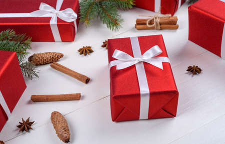 Christmas background with red gift boxes, fir tree branches, pine cones, cinnamon sticks and stars anise. Red Christmas gift boxes on white wooden background. Holiday greeting card. Flat lay top viewの写真素材