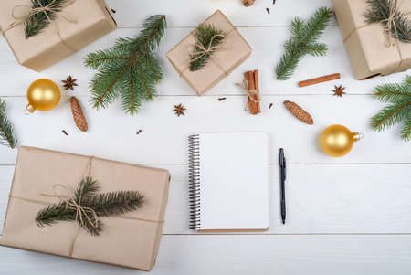 Top view of blank notebook for template design on white wooden background with xmas decorations, copy space. Christmas background with notebook for wish list or to do list and gift boxes. Flat layの写真素材
