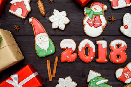 Happy new year 2018 sign symbol with red and white gingerbread cookies on dark wooden background, copy space. Top view, flat lay. Christmas cookies, santa, snowman, snowflake, cinnamon, free spaceの写真素材