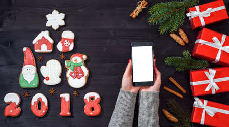 Mobile smart phone with blank screen for app presentation in woman hands, copy space. Christmas background. Christmas gifts and gingerbread cookies. Flat lay, top view. Application mock up templateの写真素材