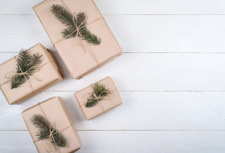 Christmas background with gift boxes wrapped in kraft paper with fir tree branches on white wooden background, free space. Holiday greeting card, copy space. Flat lay, top viewの写真素材