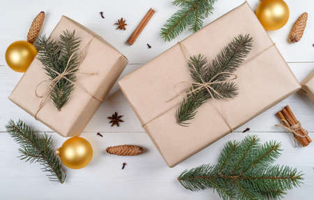 Christmas background with gift boxes wrapped in kraft paper, fir tree branches, golden glass balls, pine cones, cinnamon sticks and stars anise on white wooden background. Flat lay, top view の写真素材