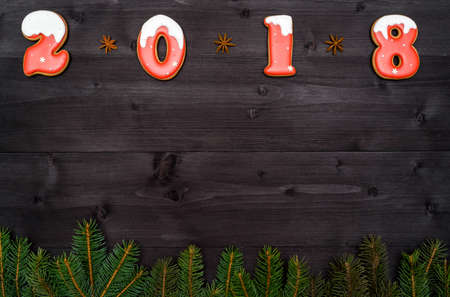 Happy new year 2018 sign symbol from red and white gingerbread cookies on dark wooden background with fir tree branches, copy space. Top view, flat lay. New Year or Christmas postcardの写真素材