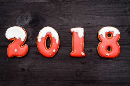 Happy new year 2018 sign symbol from red and white gingerbread cookies on dark wooden background, copy space. Top view, flat layの写真素材