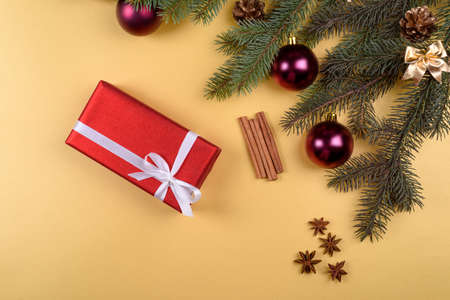 Christmas background with red gift box, fir tree branches with glass balls, pine cones, cinnamon sticks and stars anise on golden background, free space. Flat lay, top view with copy space の写真素材