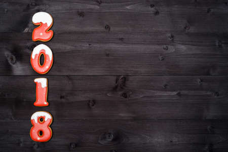 Happy new year 2018 sign symbol from red and white gingerbread cookies on dark wooden background, copy space. Top view, flat layの写真素材