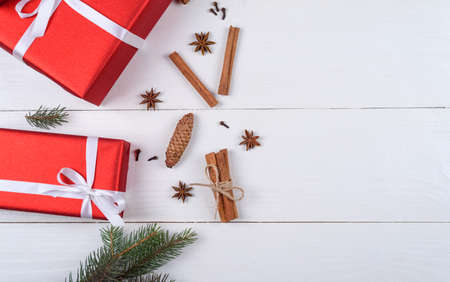 Christmas background with red gift boxes, fir tree branches, pine cones, cinnamon sticks and stars anise on white wooden background, free space. Holiday greeting card, copy space. Flat lay, top viewの写真素材