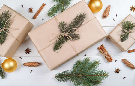 Christmas background with gift boxes wrapped in kraft paper, fir tree branches, golden glass balls, pine cones, cinnamon sticks and stars anise on white wooden background. Flat lay, top viewの写真素材